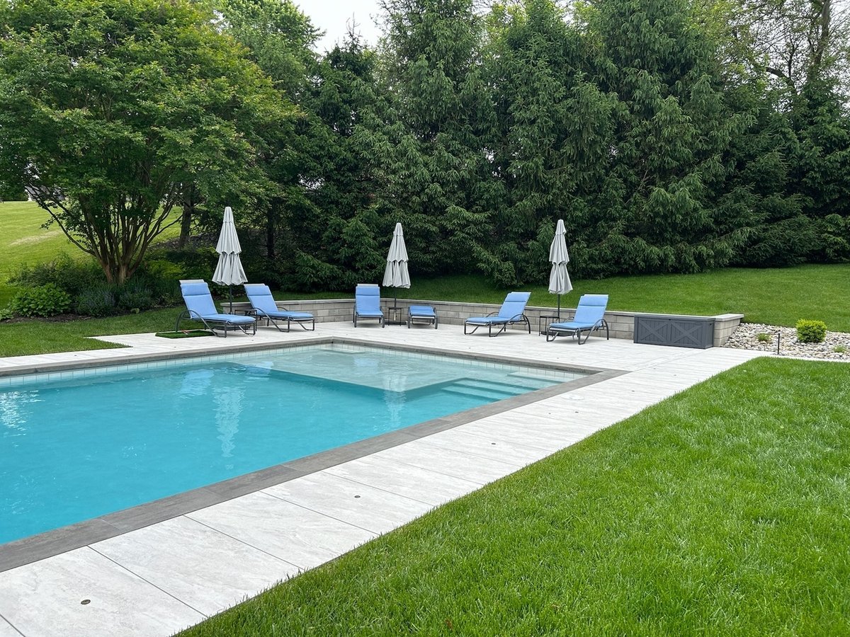Custom backyard pool patio with lounge chairs and greenery by First Class Lawncare, LLC in Wilmington, DE