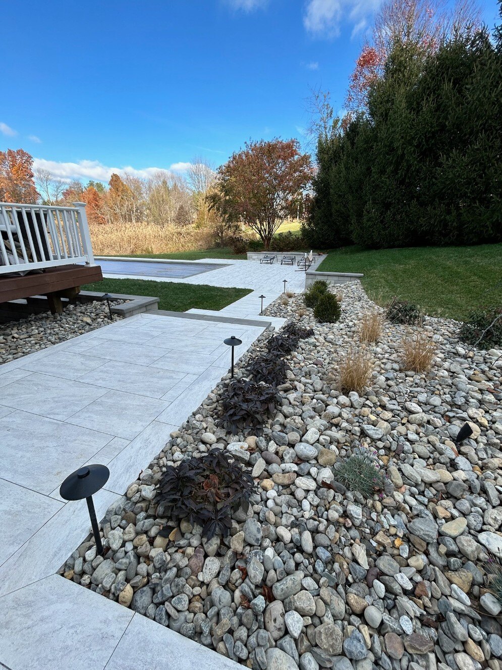 A well-designed landscape featuring porcelain pavers, drought-tolerant plants, and a modern pool area in Newark, DE by  First Class Lawncare LLC